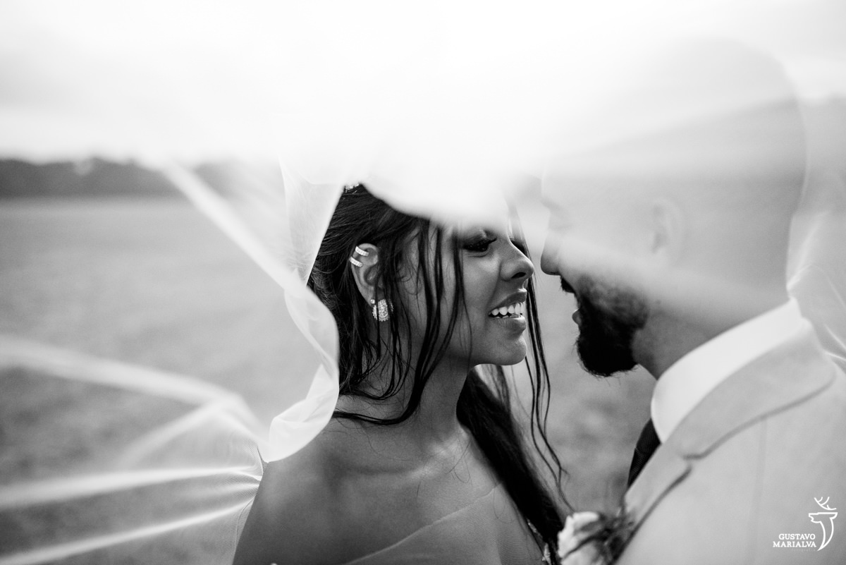noiva sorri ao olhar para noivo com o véu da noiva os cobrindo