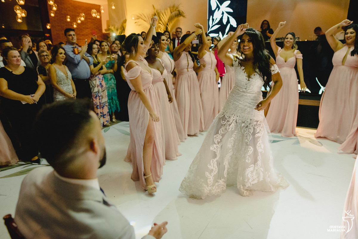 noiva dança com as madrinhas usando vestido rosa enquanto noivo observa sentado na cadeira