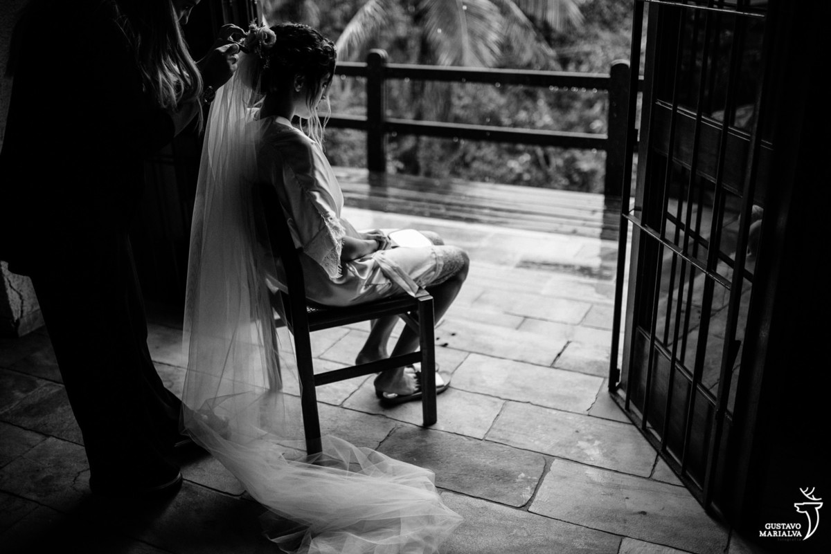 maquiadora coloca o véu na noiva que esta sentada na cadeira e usa robe branco