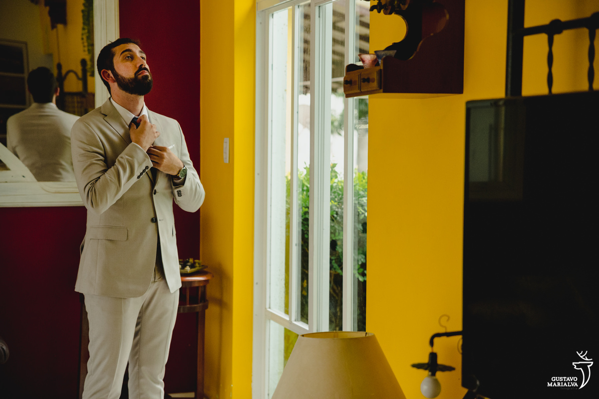 noivo arruma o nó ga gravata azul em frente a parede vermelha e amarela