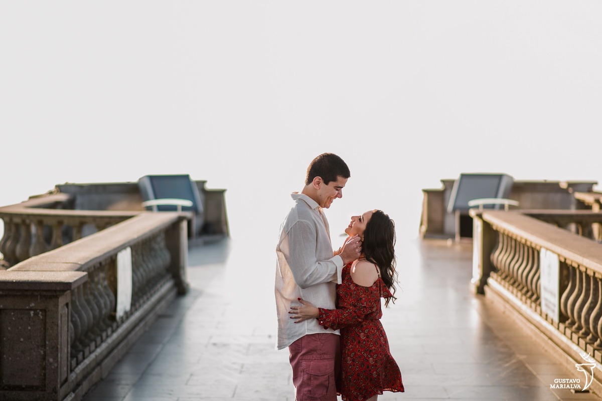 namorado usando bermuda coral e camisa branca faz carinho no rosto da noiva que usa vestido vermelho estampado