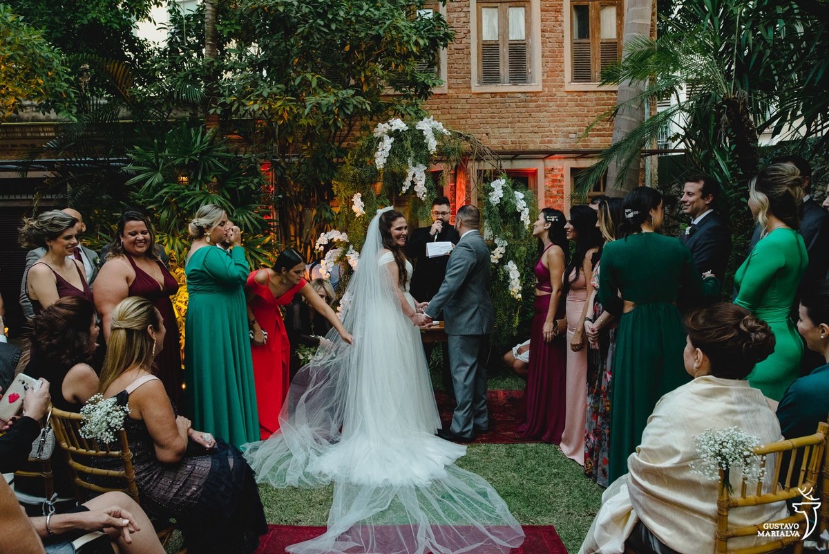 noivos de mãos dadas olham para os convidados e sorriem