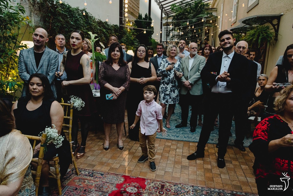 menino usando camisa social rosa faz careta enquanto convidados observam a cerimônia de casamento 