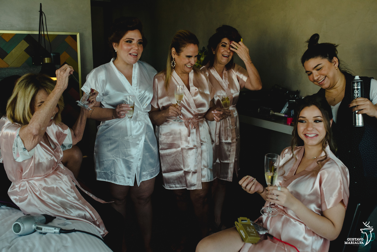 noiva conversa com as tias que usam robe rosa enquanto prima arruma o cabelo