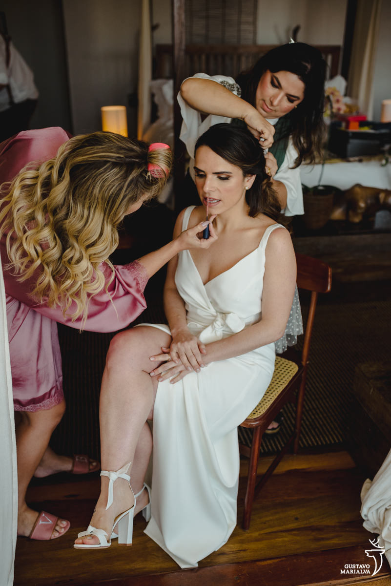 noiva usando vestido de noiva da carol hungria é maquiada enquanto assistente arruma o cabelo