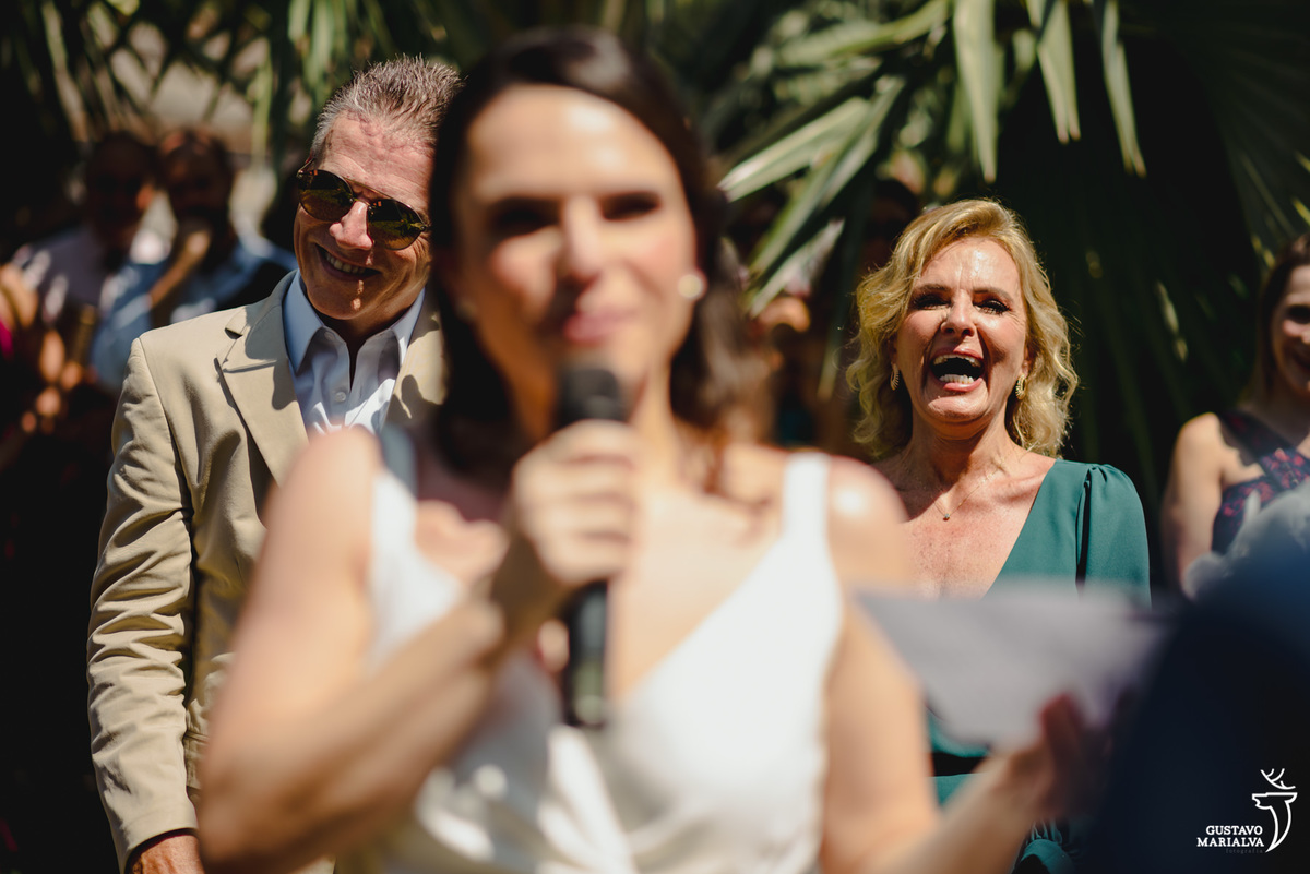 noiva lê os votos enquanto é observada pela mãe que usa vestido verde e sorri