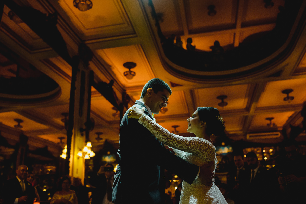 noivos dançam na festa de casamento com luzes laranja do teto destacadas