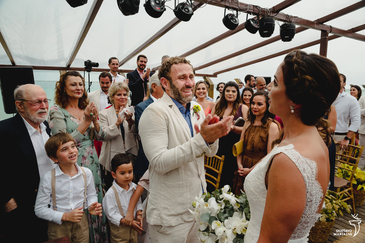 noivo usando terno caqui aplaude a noiva e é acompanhado pelos convidados