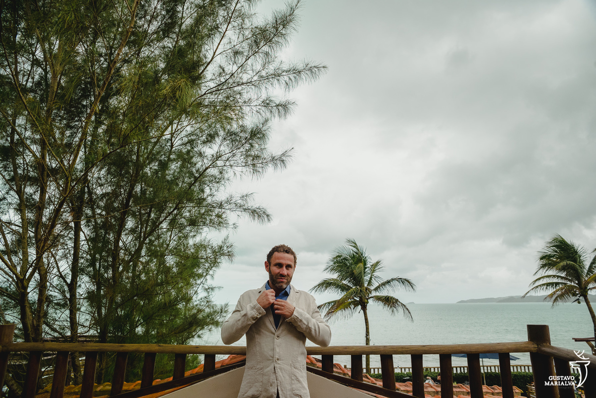 noivo arruma a gola da camisa azul em frente a praia rasa, em búzios