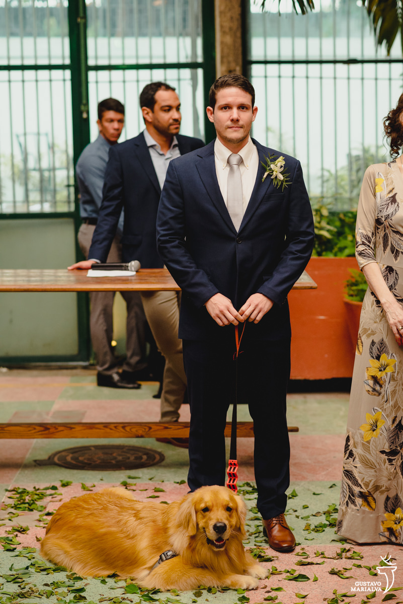 noivo usando terno azul sorri ao ver a noiva entrada e cachorro golden filhote observa