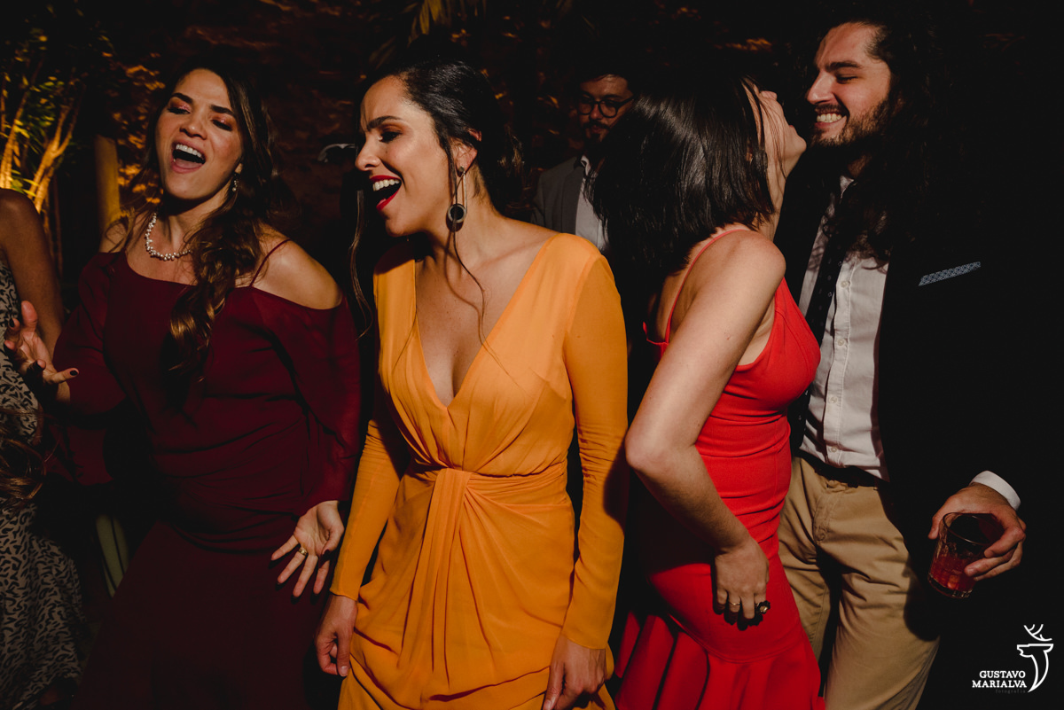 amigas usando vestido laranja e vinho dançam enquanto casal namora ao lado