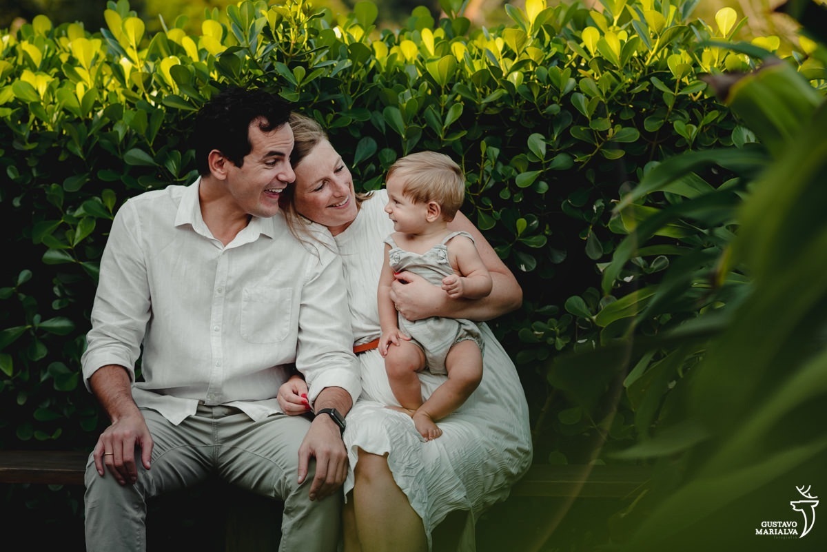 familia usando roupas brancas e beges posam para foto com paredes de plantas verdes em volta