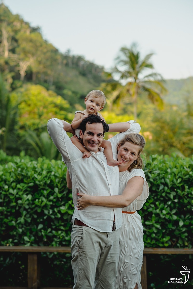 familia usando roupas brancas e beges posam para foto com paredes de plantas verdes em volta