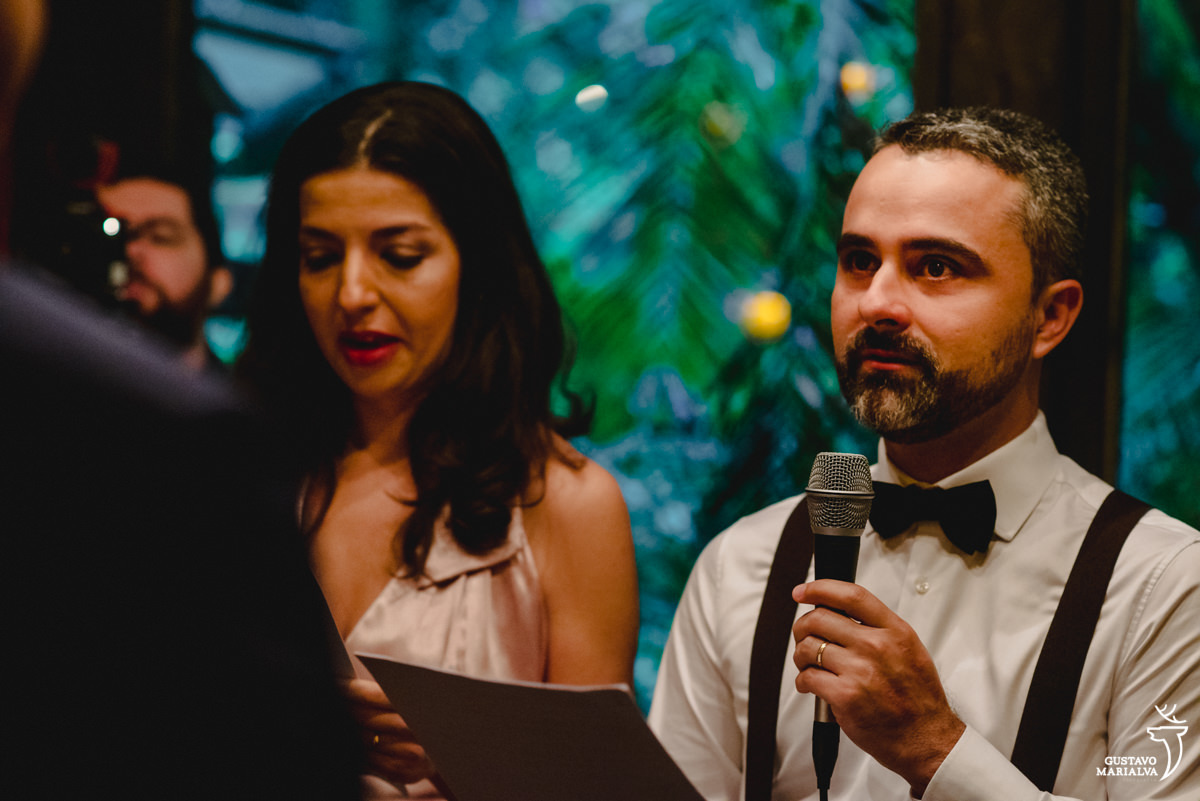 padrinho usando camisa branca, suspensório e gravata borboleta se emociona ao ler a celebração do casamento