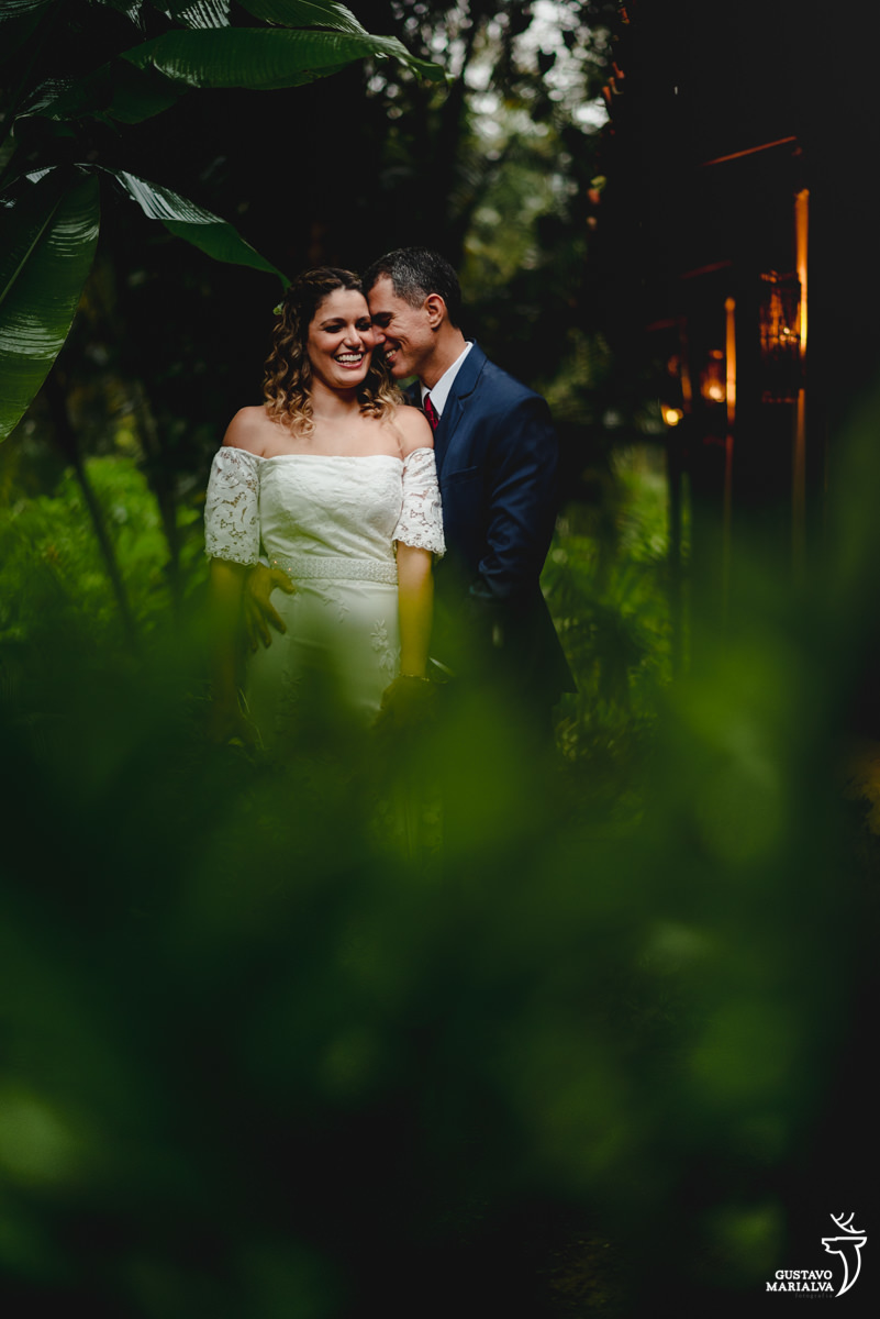 noivos se abraçam durante retratos de casamento em frente a plantas verdes