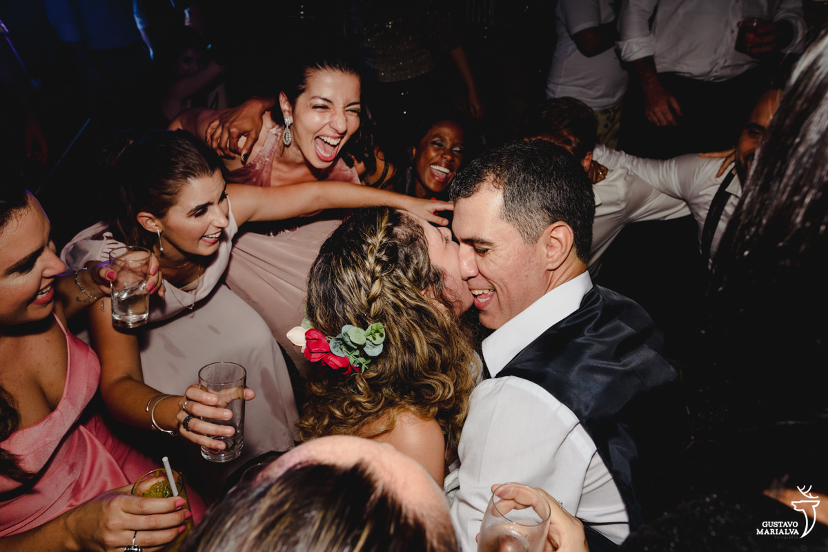 noivos dançam agachados enquanto madrinhas de vestido rosa sorriem animadas