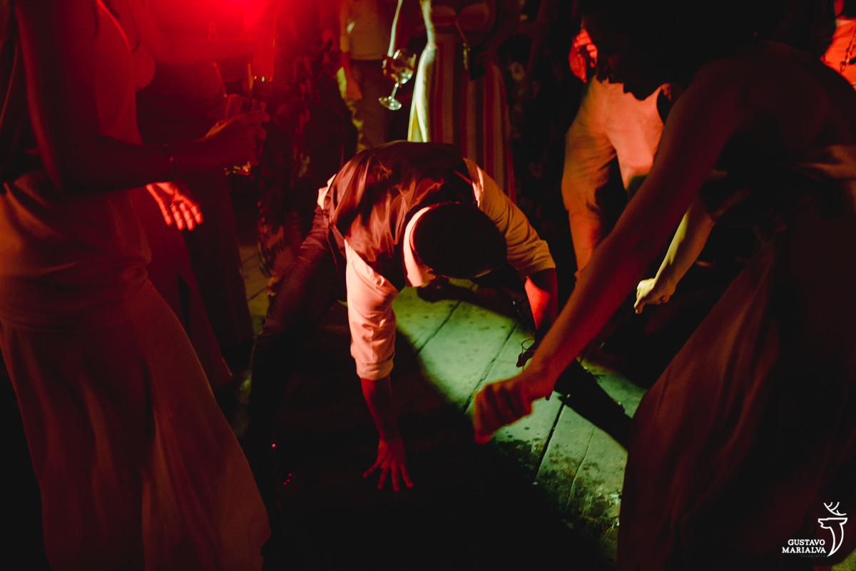 noivo dança com as mãos no chão iluminado por luz vermelha e observado por madrinhas