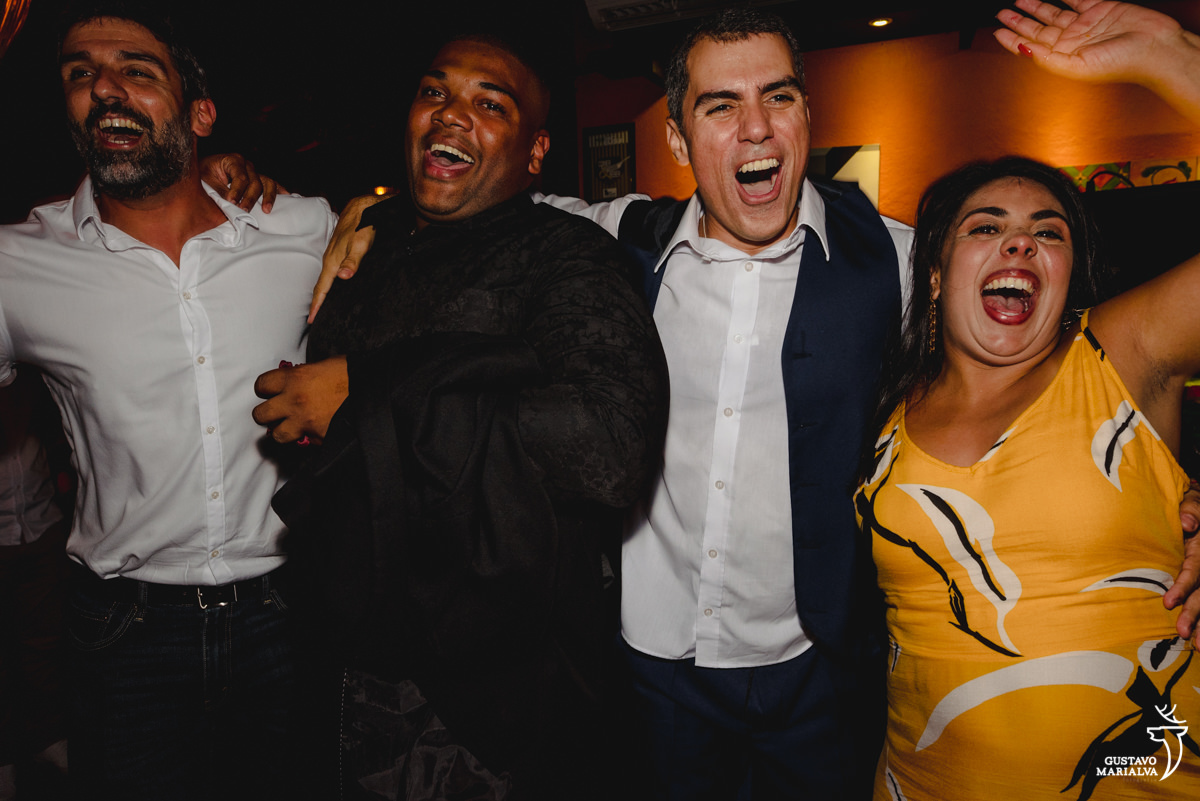 noivo pula abraçado a amiga de vestido amarelo e rapaz de camisa preta