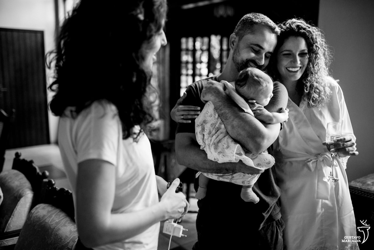 noiva abraça padrinho que segura a filha bebe no colo enquanto é observado pela esposa