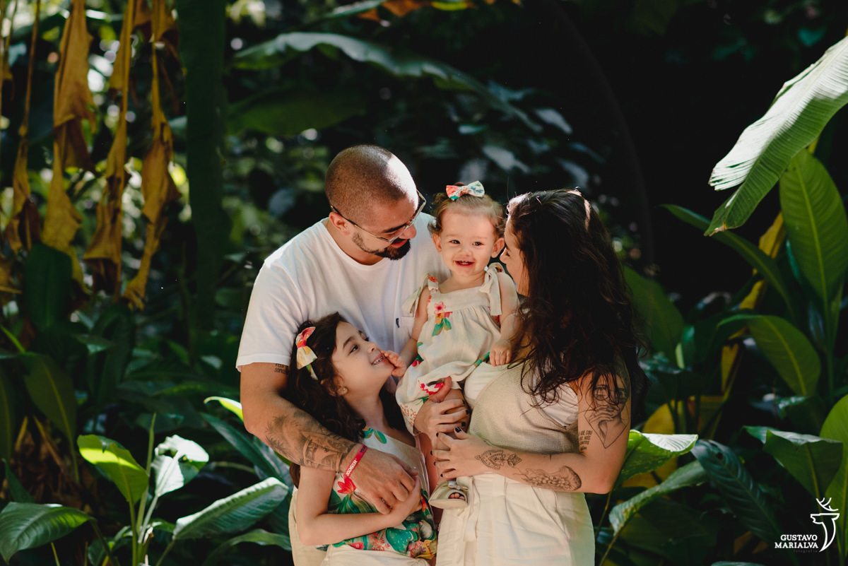 família usando roupa bege e florida se abraça no meio da mata do parque lage