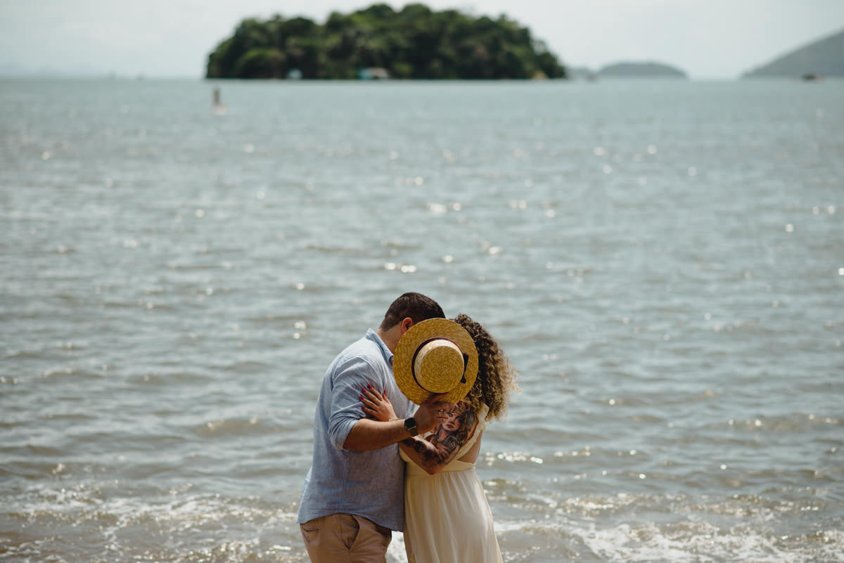 casal se beija escondido por chapéu de palha em frente a praia