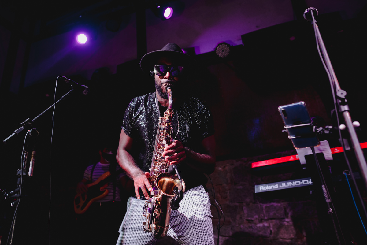 saxofonista de camisa preta com brilhos, calça branca e chapéu preto toca durante a festa de casamento  