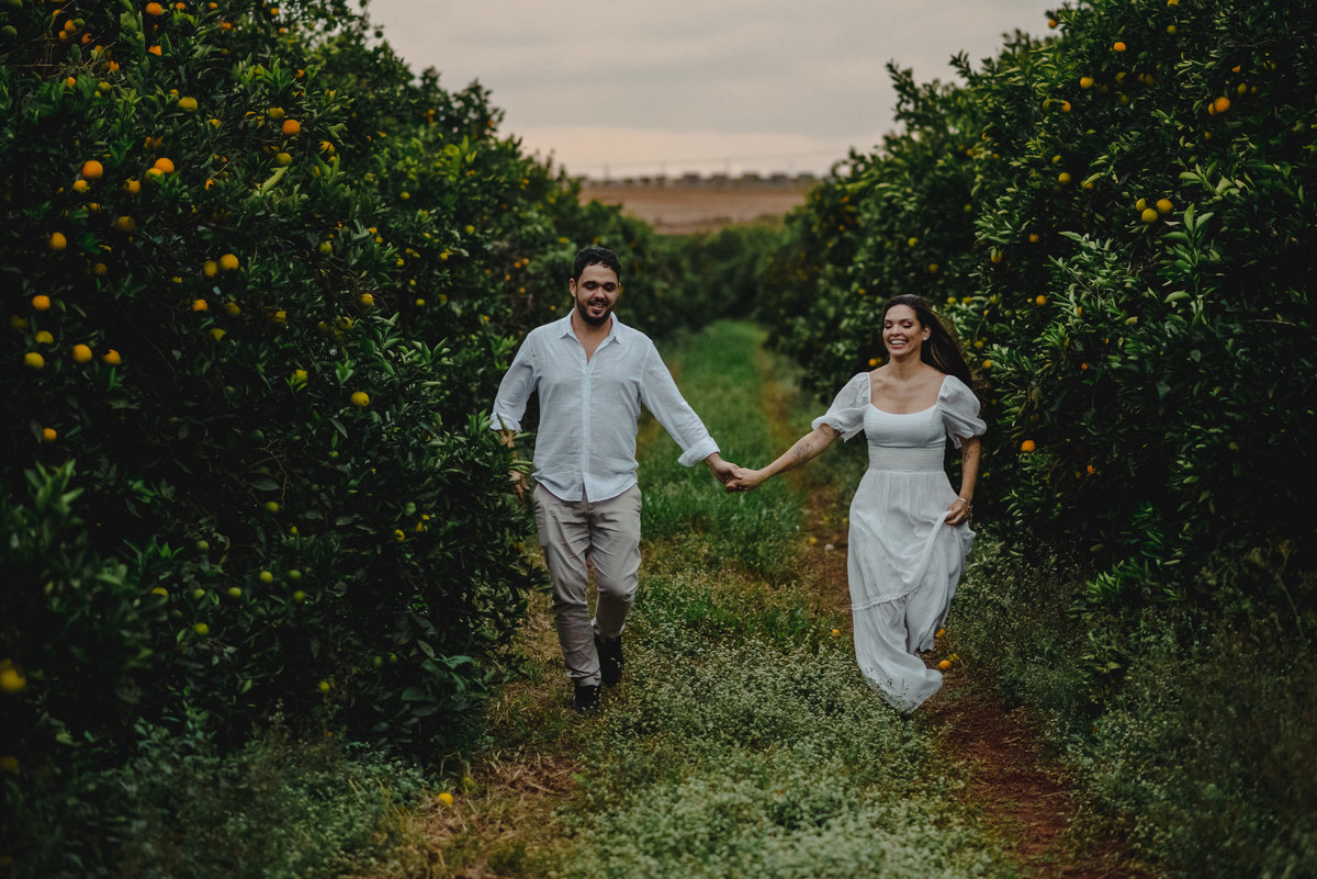 casal de roupa branca corre no meio de plantação de laranjas em Holambra 