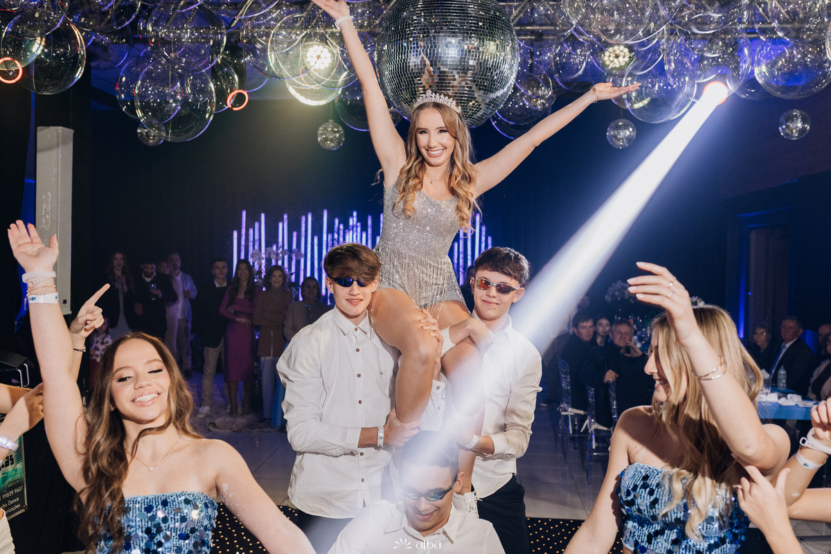 Diuli sendo levantada na pista pelos meninos com braços erguidos e luzes de festa, na sua comemoração de 15 anos no Refinatta, fotografada pelo Alba Estúdio