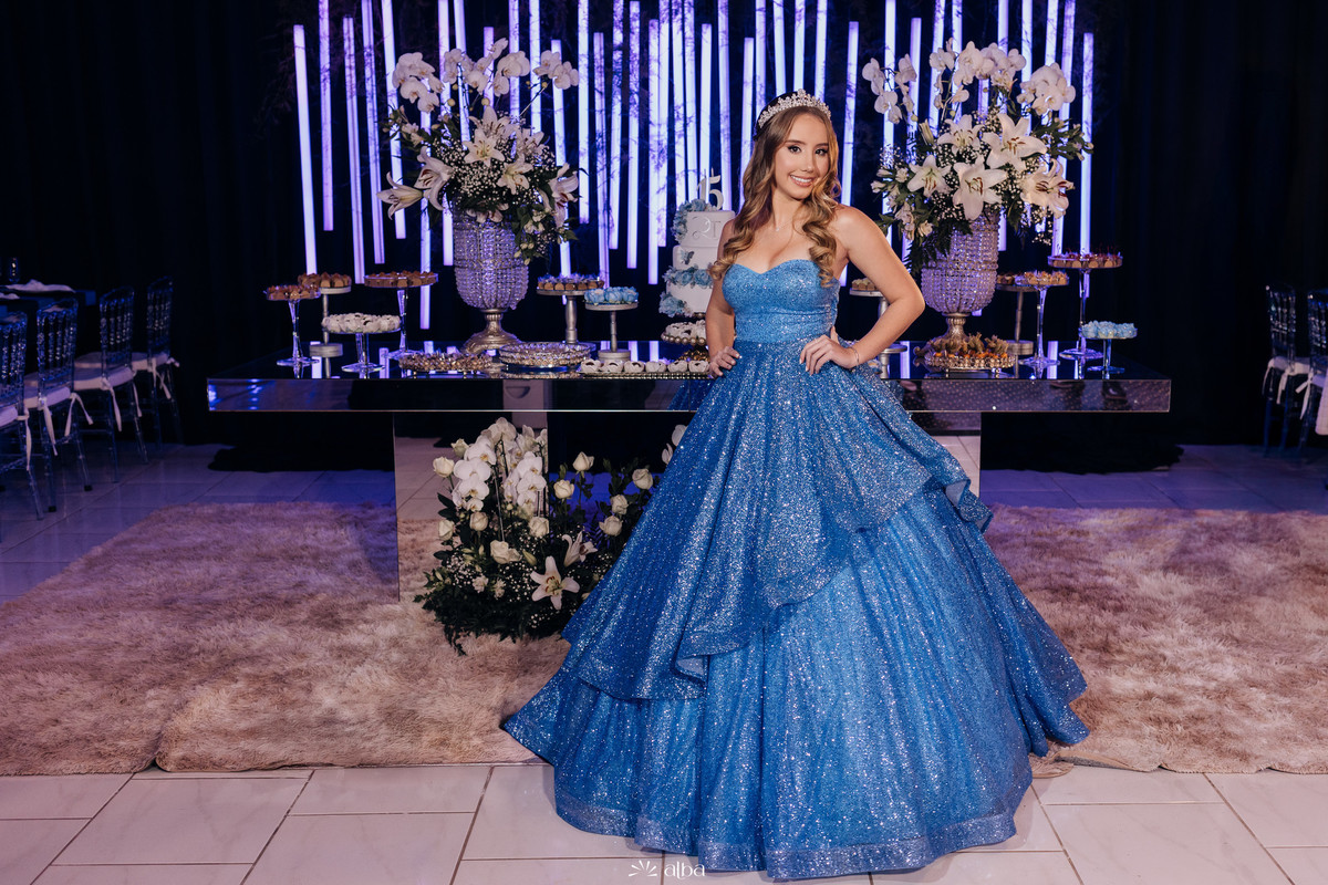 Debutante Diuli em sua festa de 15 anos com vestido azul brilhante, decorada com flores brancas e luzes neon no Refinatta, Venâncio Aires. Foto por Alba Estúdio.