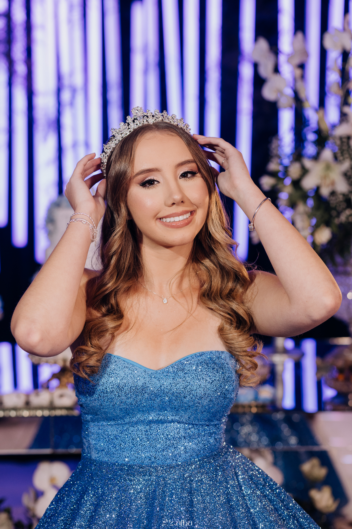 Debutante Diuli ajustando a tiara, usando vestido azul cintilante na festa de 15 anos no Refinatta, Venâncio Aires. Foto por Alba Estúdio.