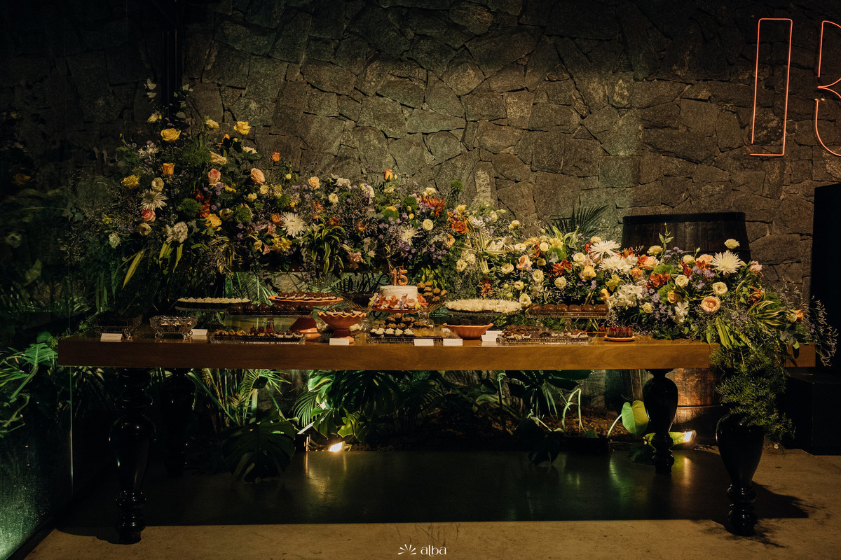 Mesa de doces exuberante com flores e o bolo dos 15 anos de Julia, decorando a festa no Roll em Lajeado. Foto por Alba Estúdio.