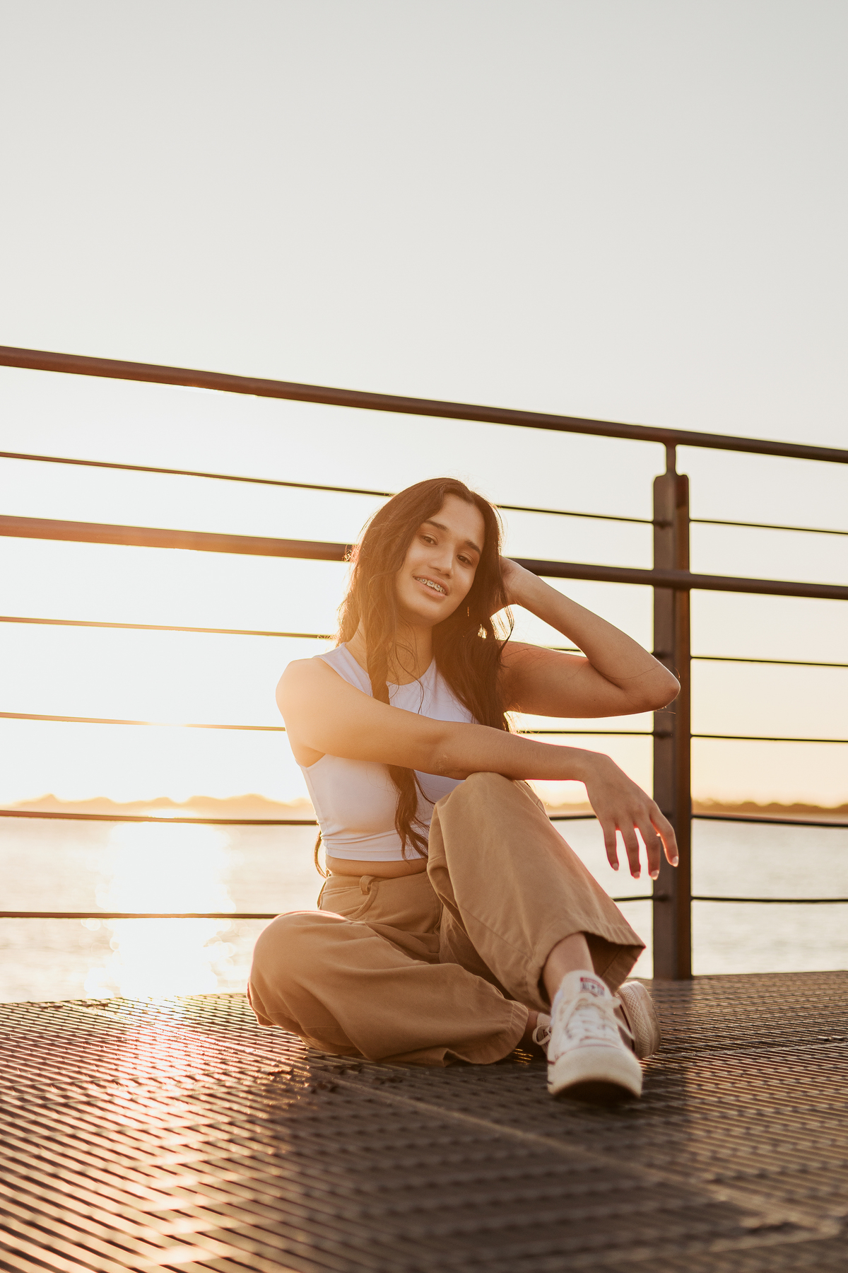 Debutante posando sentada no pôr do sol no Guaíba, com clima leve e expressão serena em ensaio de 15 anos.