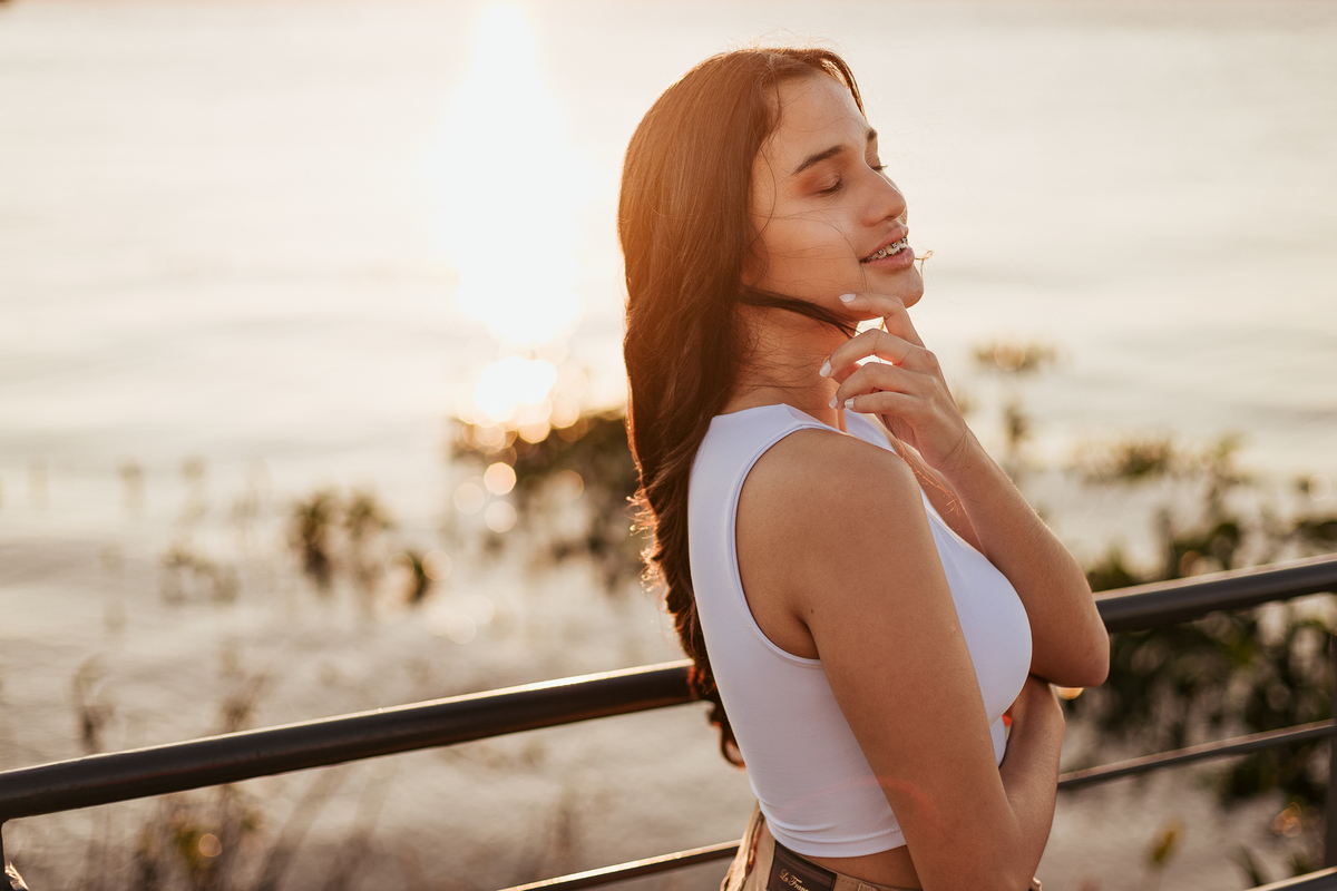 Ensaio fotográfico de debutante com expressão suave e luz do sol refletindo nas águas do Guaíba em Porto Alegre.