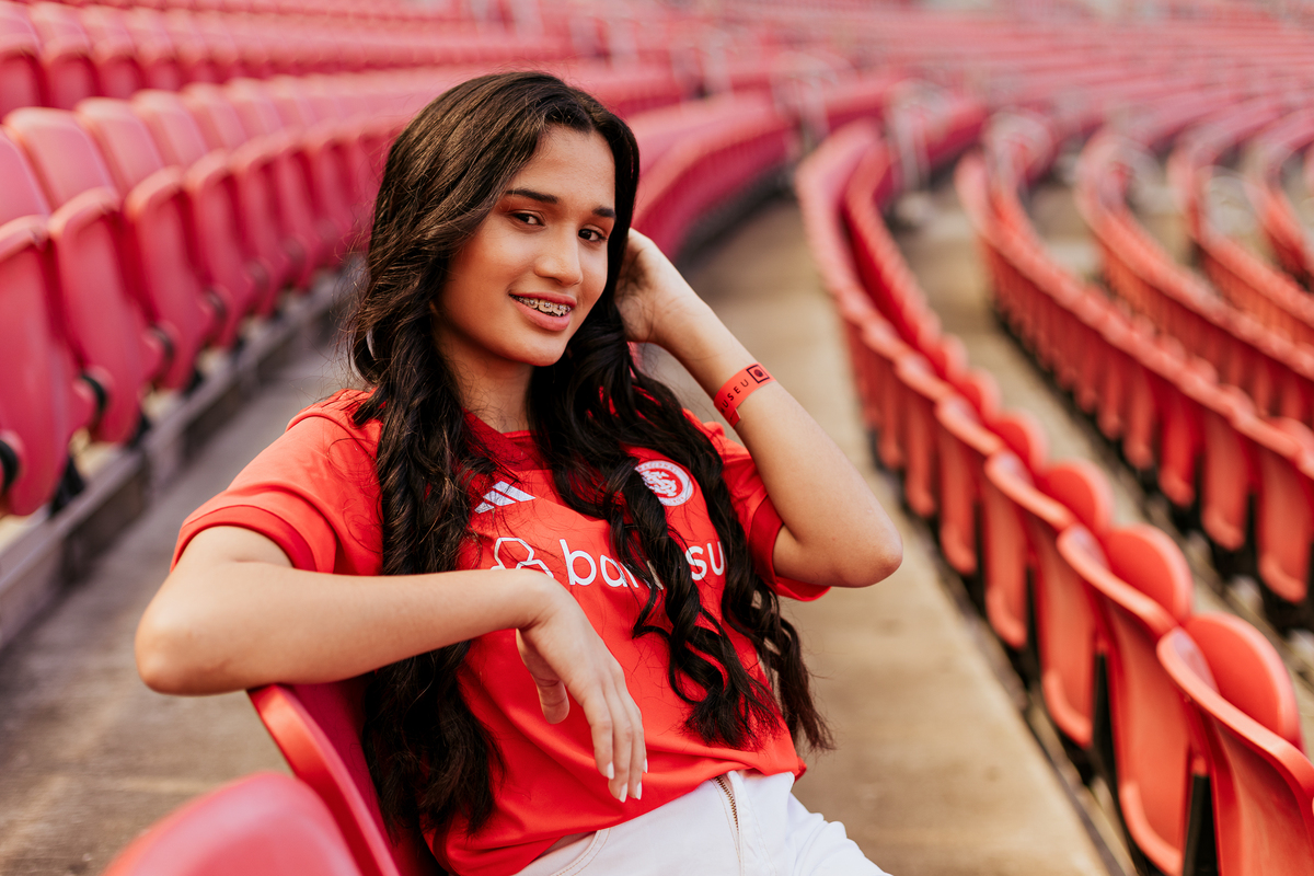 Debutante sentada entre as cadeiras vermelhas do Beira-Rio, usando camisa do Internacional no ensaio de 15 anos em Porto Alegre – foto por Alba Estúdio.