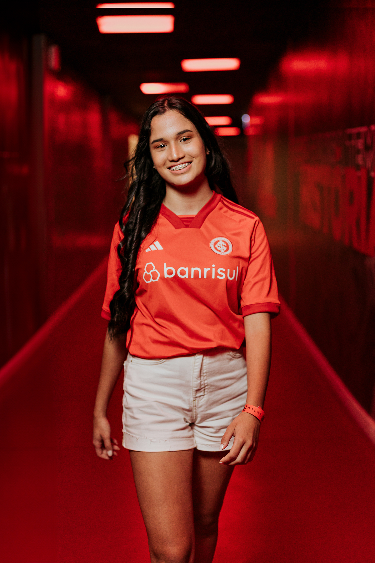 Djuly em ensaio de 15 anos no Beira-Rio, em Porto Alegre, usando camisa do Inter e sorrindo em corredor iluminado de vermelho – foto por Alba Estúdio.