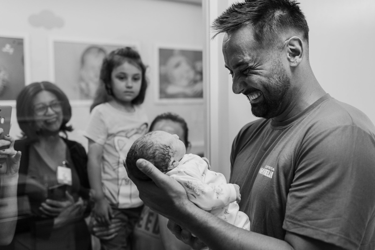 Pai emocionado segurando o bebê recém-nascido diante da família em Lajeado – Hospital Bruno Born – Alba Estúdio