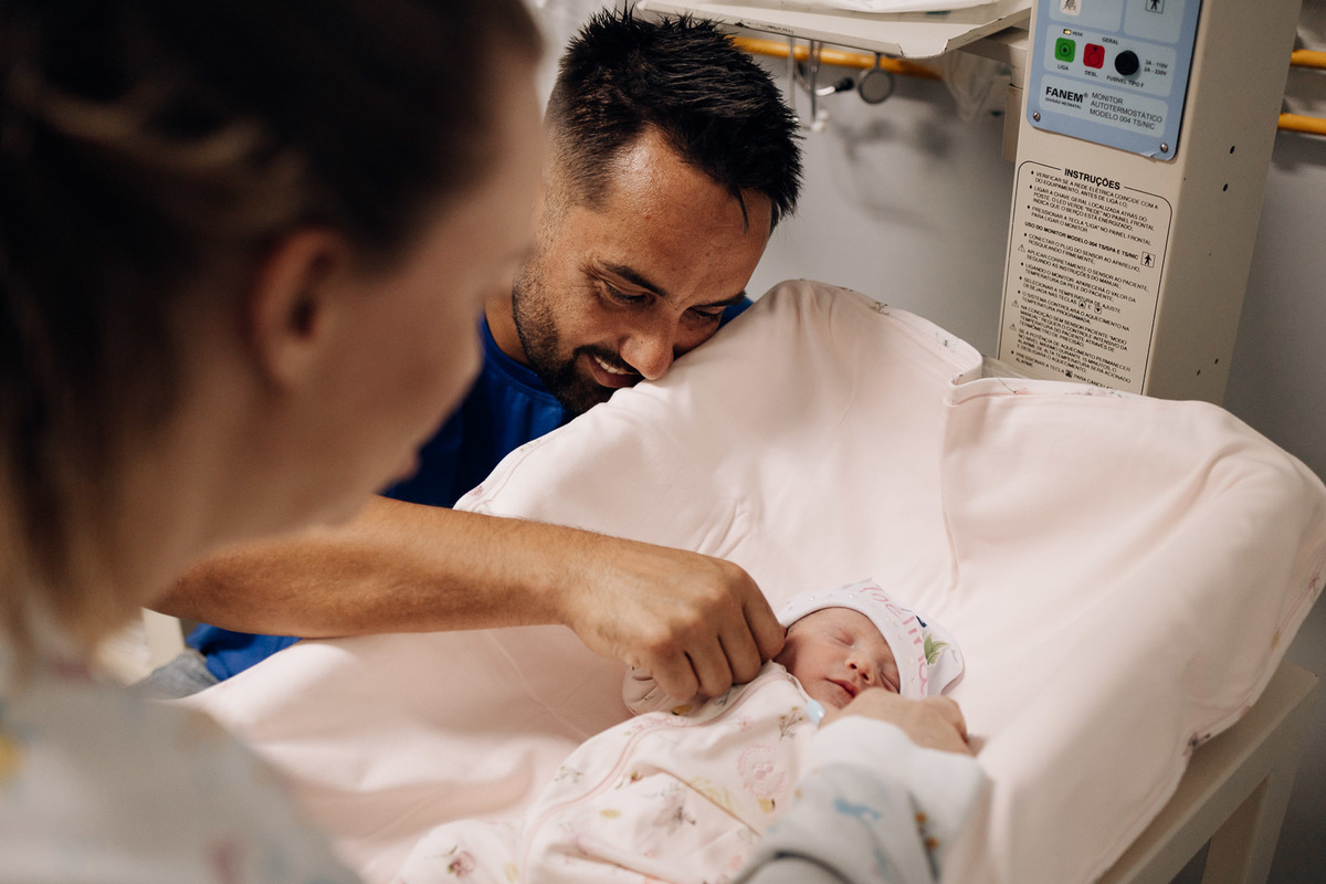 Pai emocionado olhando para o bebê recém-nascido no berço aquecido do Hospital Bruno Born em Lajeado – fotografia de parto por Alba Estúdio