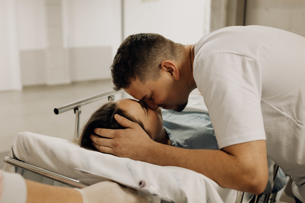 Beijo emocionado entre o casal no corredor do hospital, a caminho do nascimento do bebê.