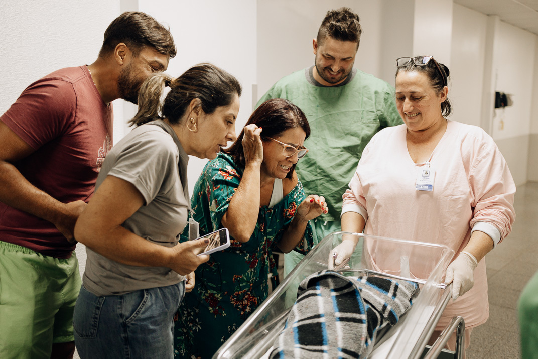 “Familiares emocionados observam o bebê enrolado em manta no berço do corredor do Hospital Bruno Born em Lajeado”