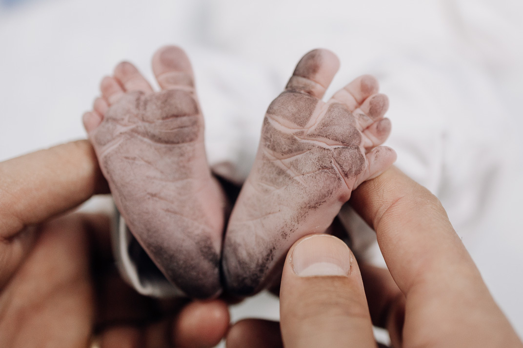 “Close‑up dos pés enrugados do bebê recém‑nascido sendo carinhosamente segurados”