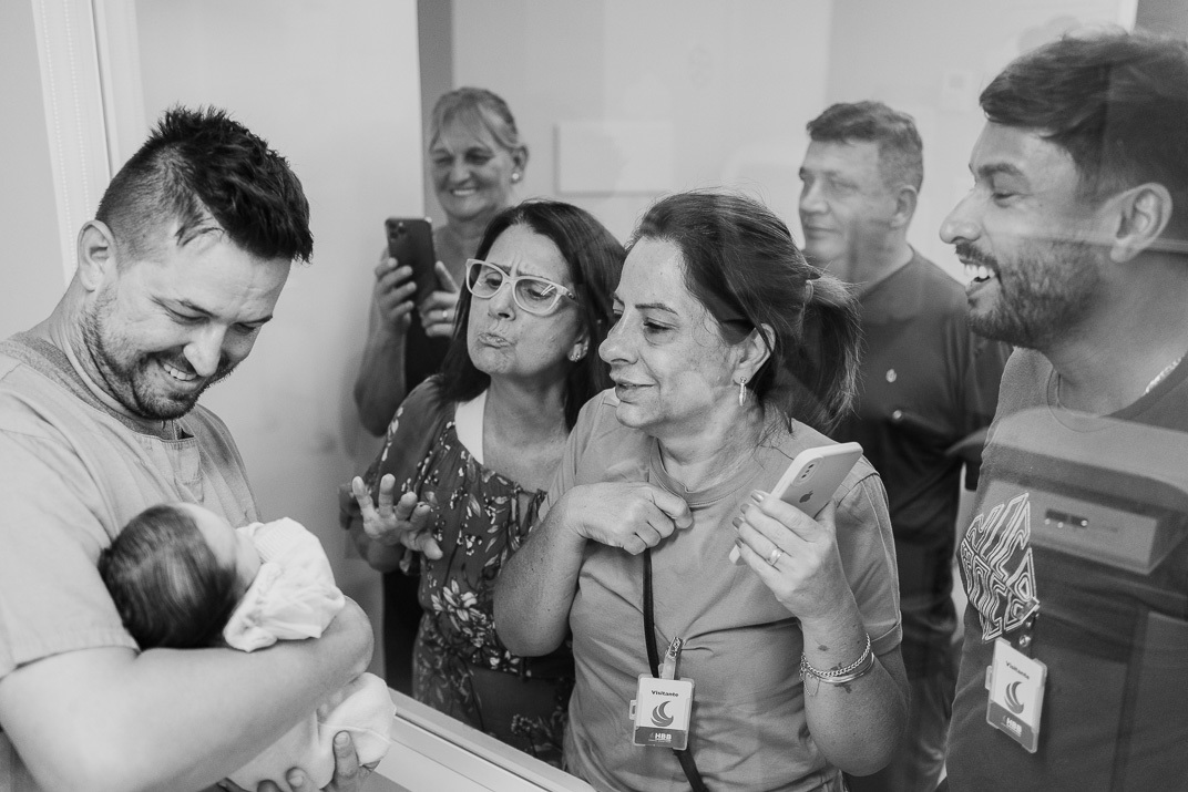 “Pai sorri afetuoso enquanto faz carinho no recém‑nascido deitado no berço da maternidade”