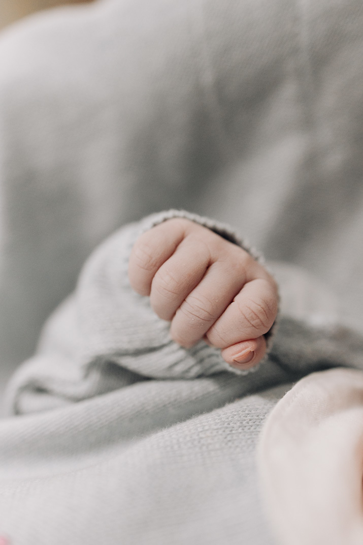 “Punho do bebê recém‑nascido fechado contra a roupa de malha, em close minimalista”