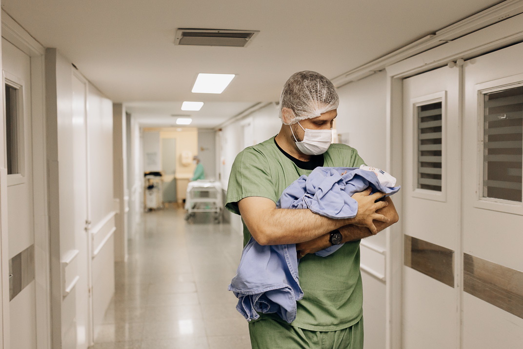 Pai caminha pelos corredores do Hospital Bruno Born carregando o bebê recém‑nascido enrolado em manta