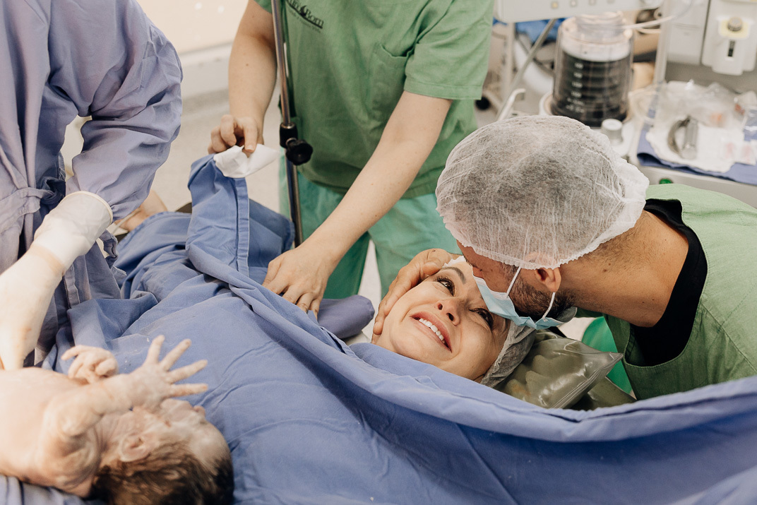 Pai beijando ternamente a testa da mãe logo após a cesária