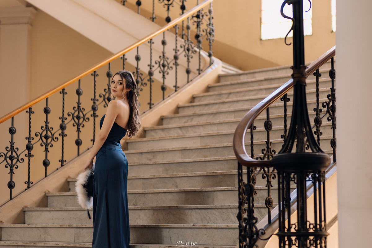 Retrato de corpo inteiro em vestido azul na escadaria de mármore com gradil de ferro da UFRGS.