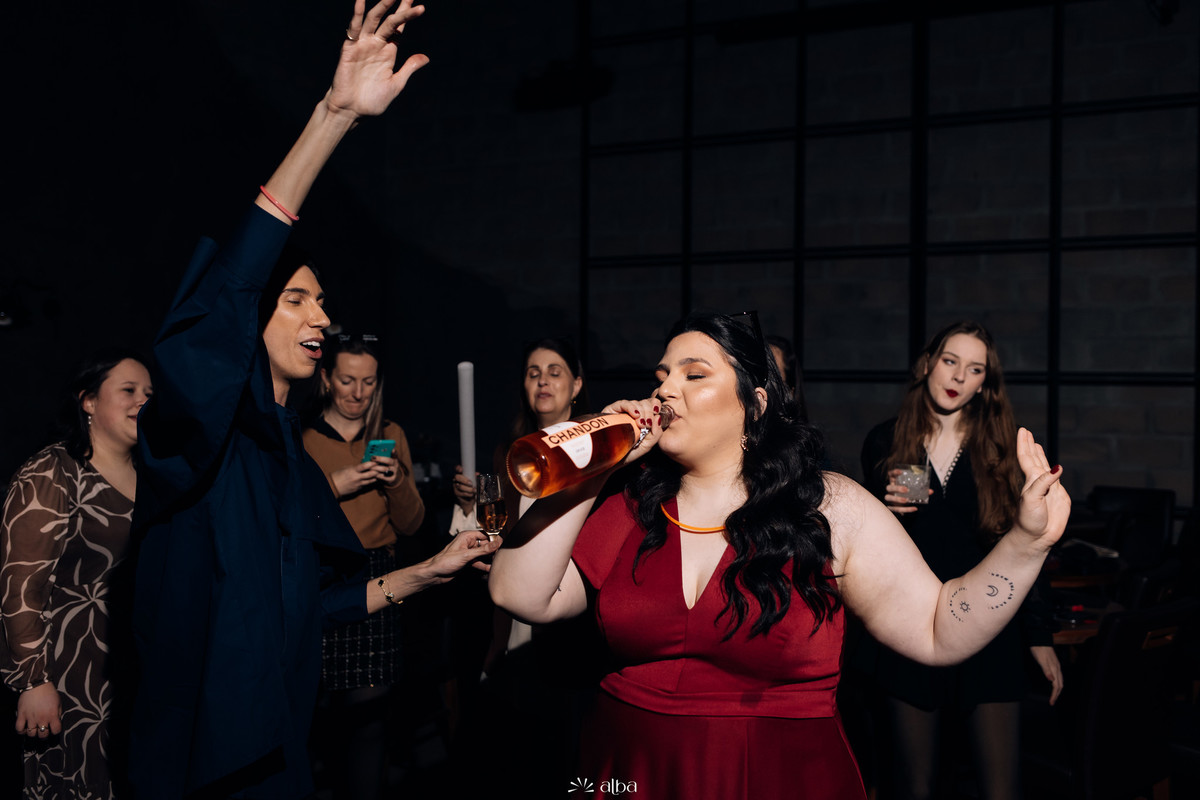 Carol canta com as amigas usando bastões de LED como microfone na festa de formatura no Bierdron, Lajeado; energia alta, vestido vermelho e muita diversão.