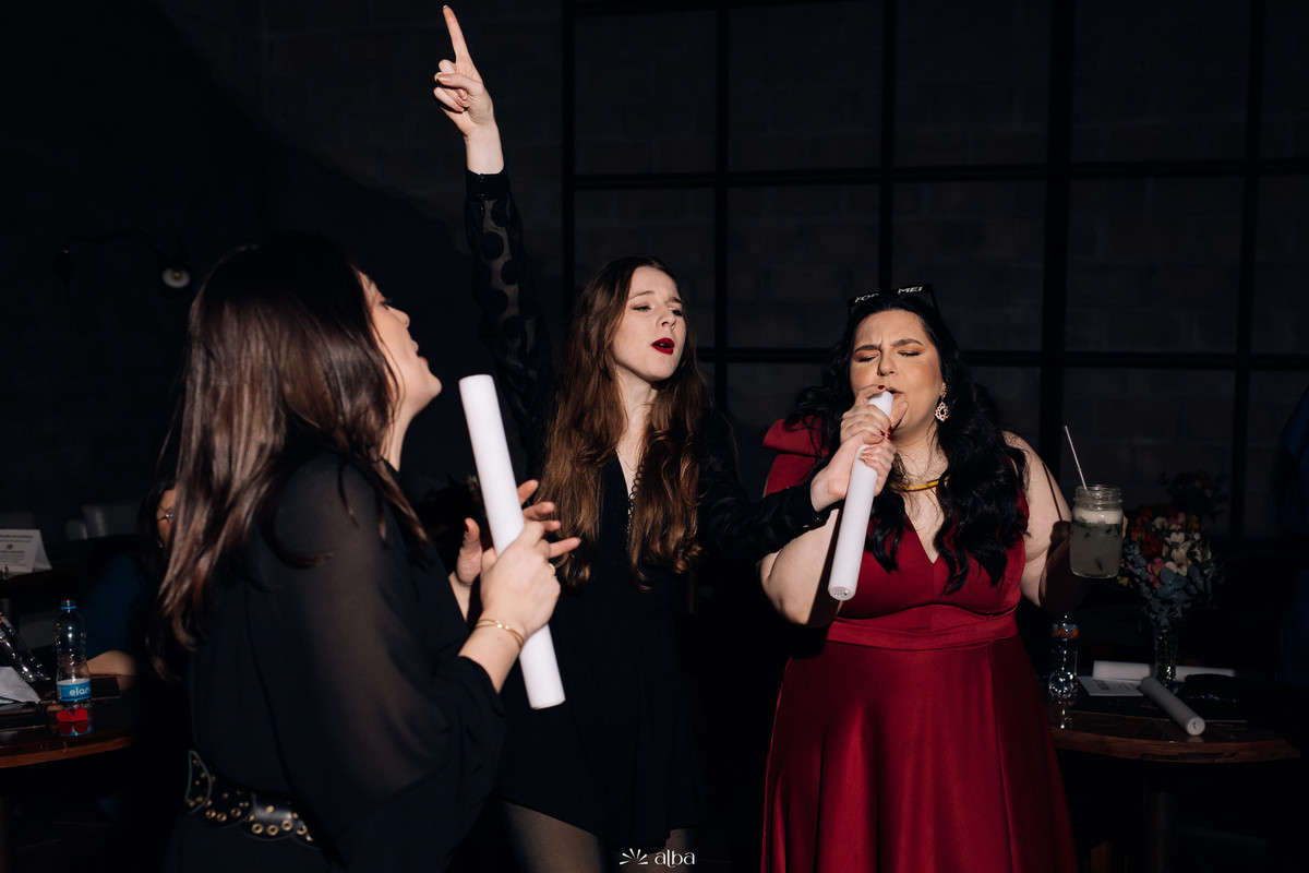 Carol bebe Chandon rosé ao lado dos amigos na pista durante sua festa de formatura no Bierdron, em Lajeado; clima de celebração, vestido vermelho e sorrisos.