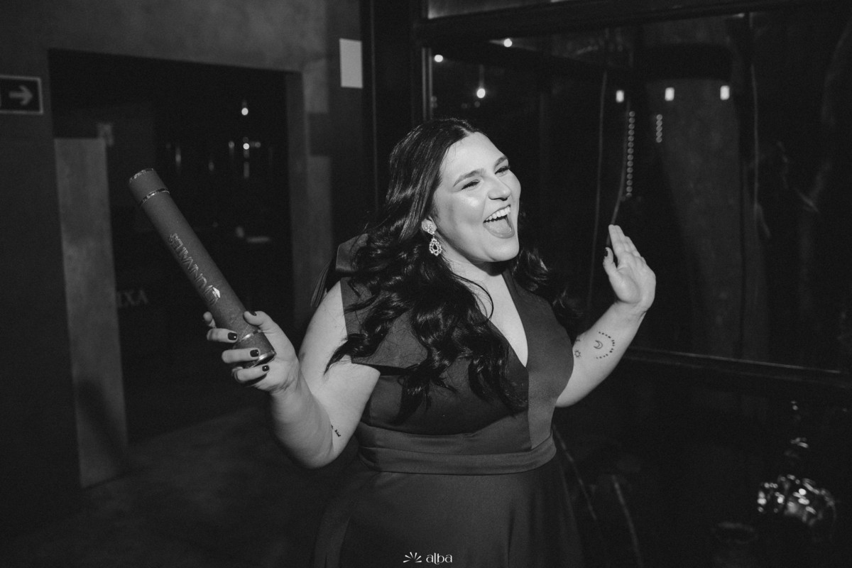 Close em P&B da Carolina comemorando com o canudo na mão durante a festa de formatura.