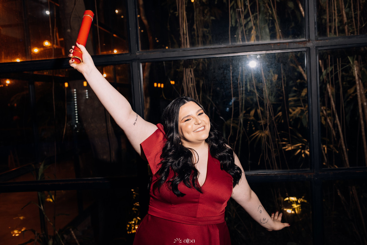 Carolina erguendo o canudo e sorrindo diante das janelas do Bierdron à noite.