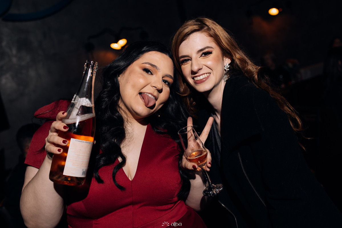 Carolina e amiga se divertindo, com garrafa e taça, na pista da formatura.